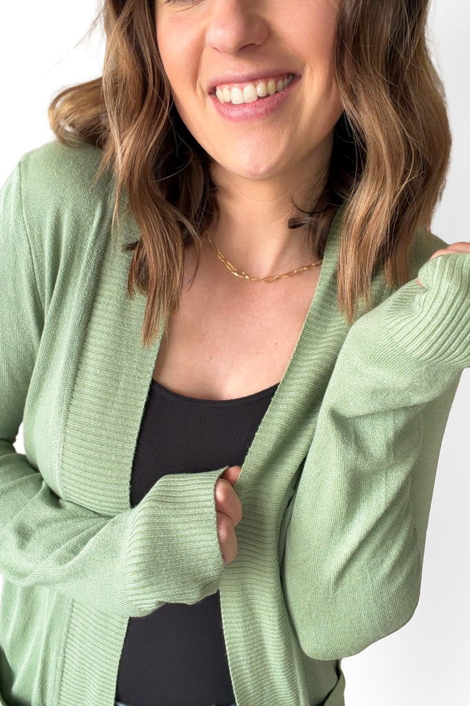 Woman wearing a light green cardigan over a black top on a white background