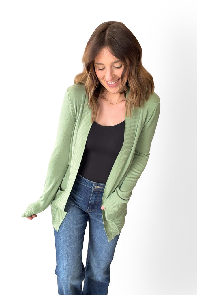 Woman wearing a light green cardigan over a black top and blue jeans on a white background