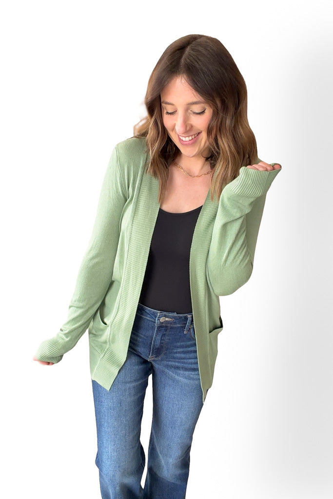 Woman wearing a light green cardigan over a black top and blue jeans on a white background