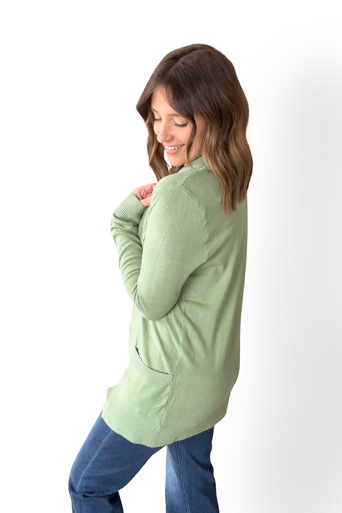 Woman wearing a light green sweater and blue jeans on a white background