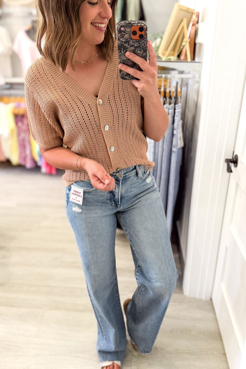 woman taking a selfie in a clothing boutique wearing a light mocha button front sweater cardigan with blue jeans and white sandals
