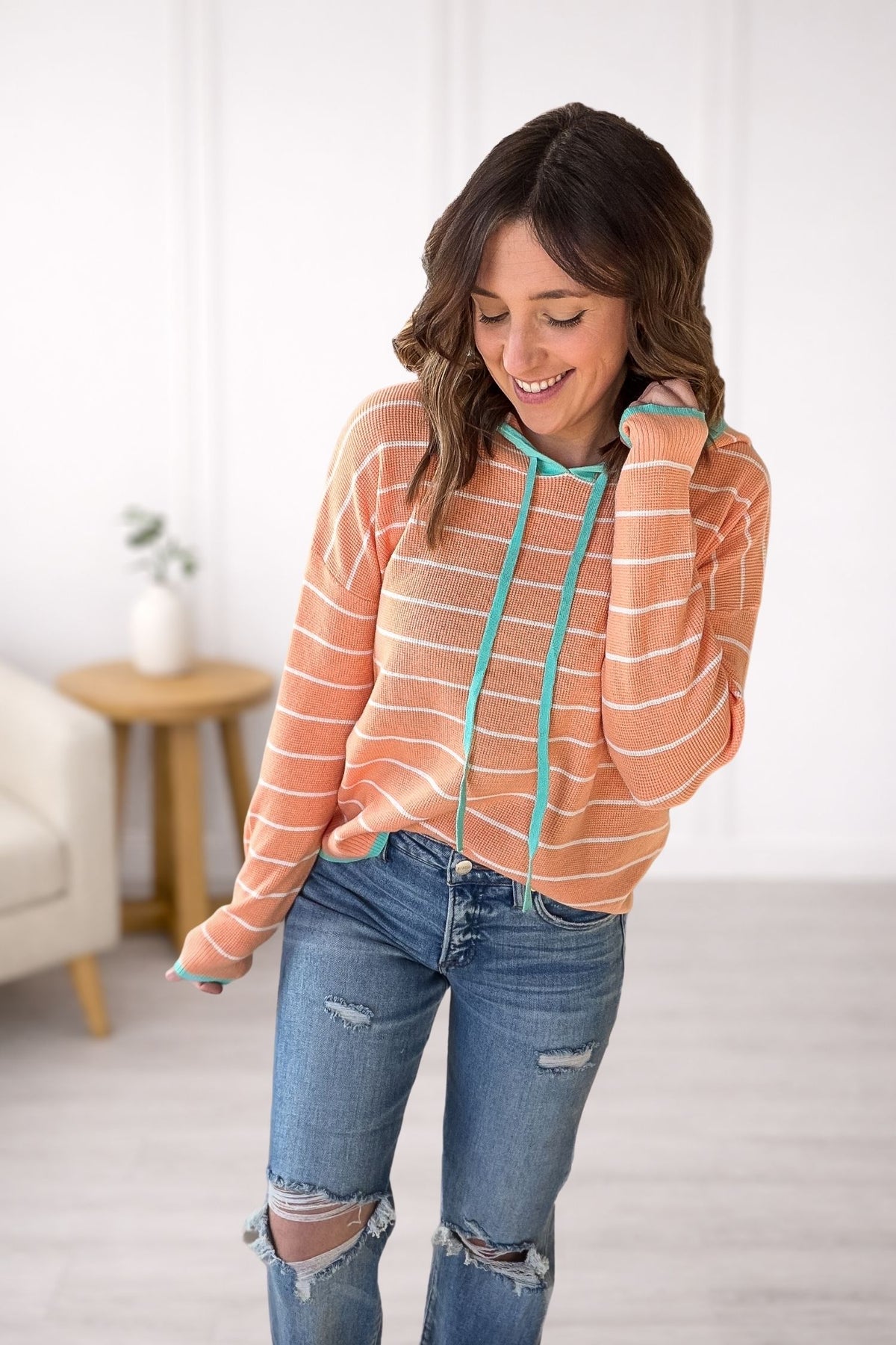 Woman wearing a striped hoodie and jeans in a room with a white wall and a small table.