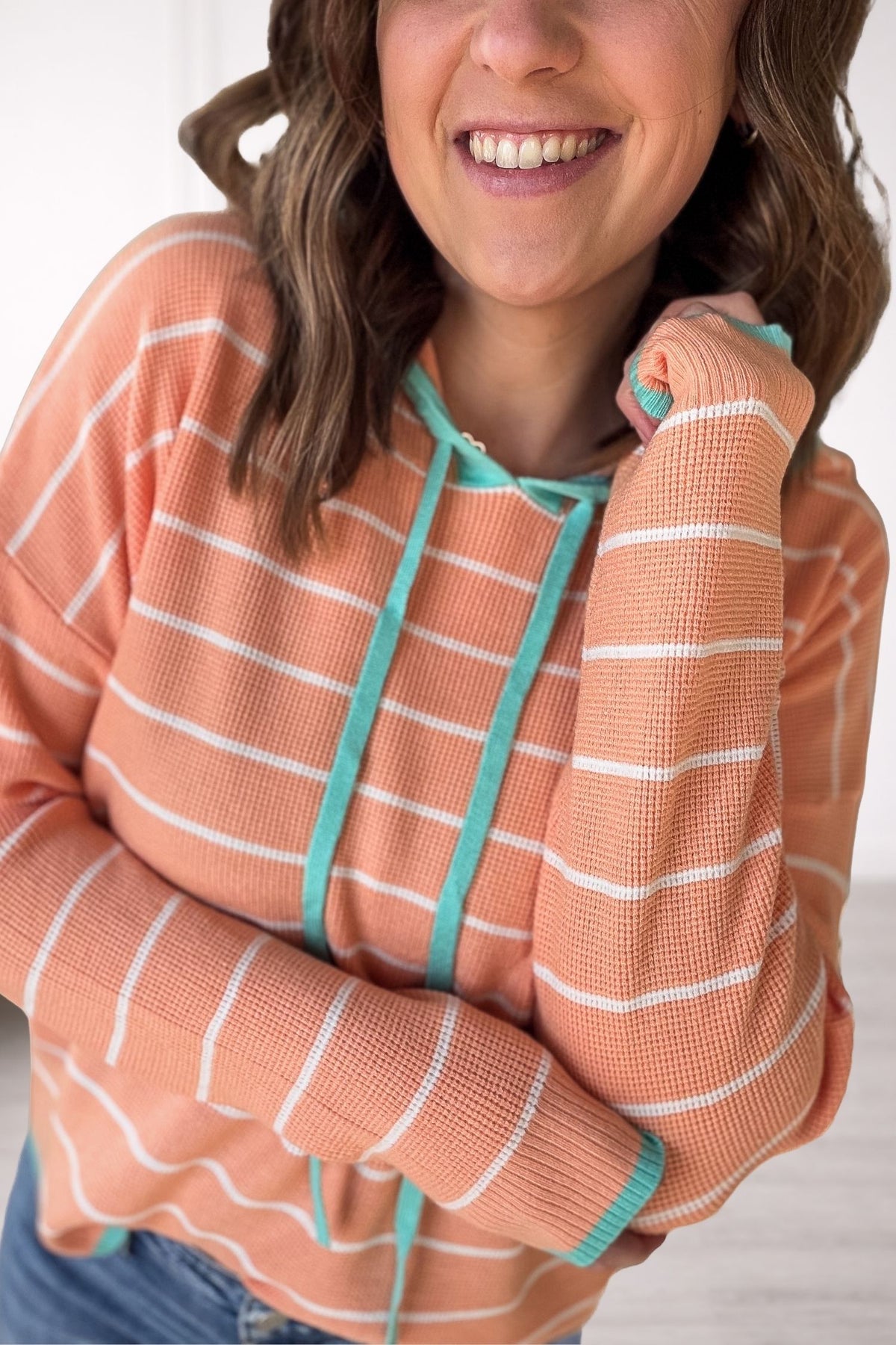 Person wearing a light orange-colored hoodie with white stripes and turquoise drawstrings, smiling.