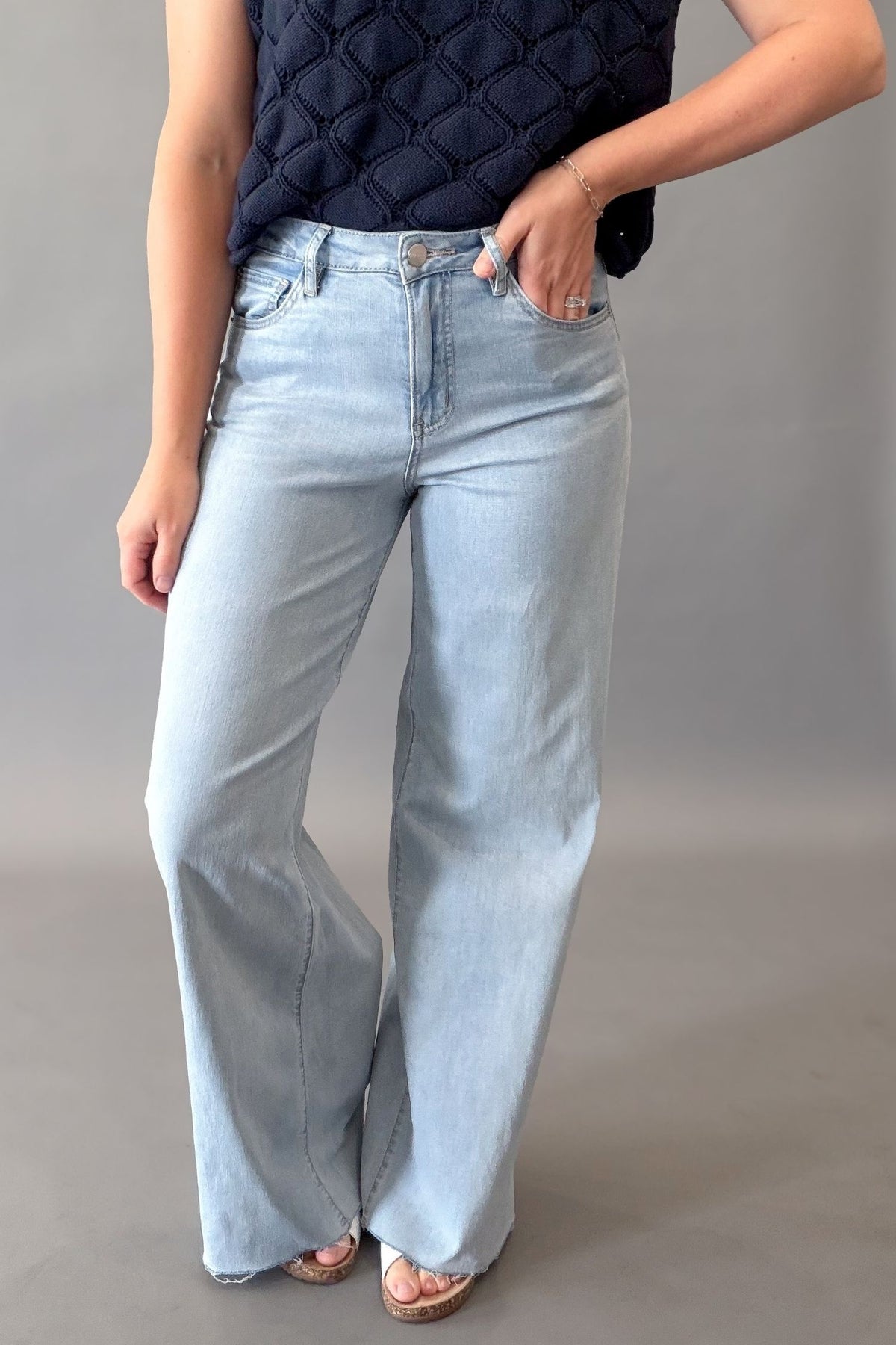 A woman wearing light-wash wide-leg Mica denim jeans with a dark navy quilted sleeveless top, standing against a plain gray studio background.