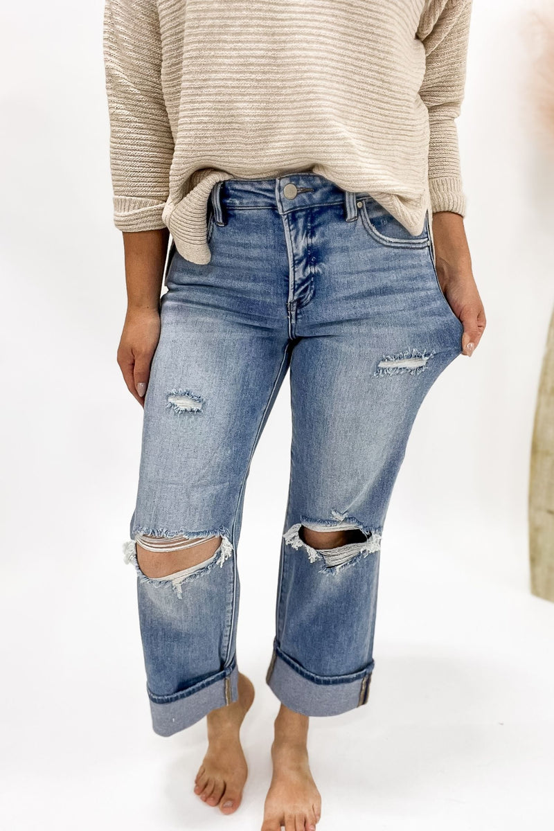 Person wearing ripped blue jeans and a beige sweater on a white background