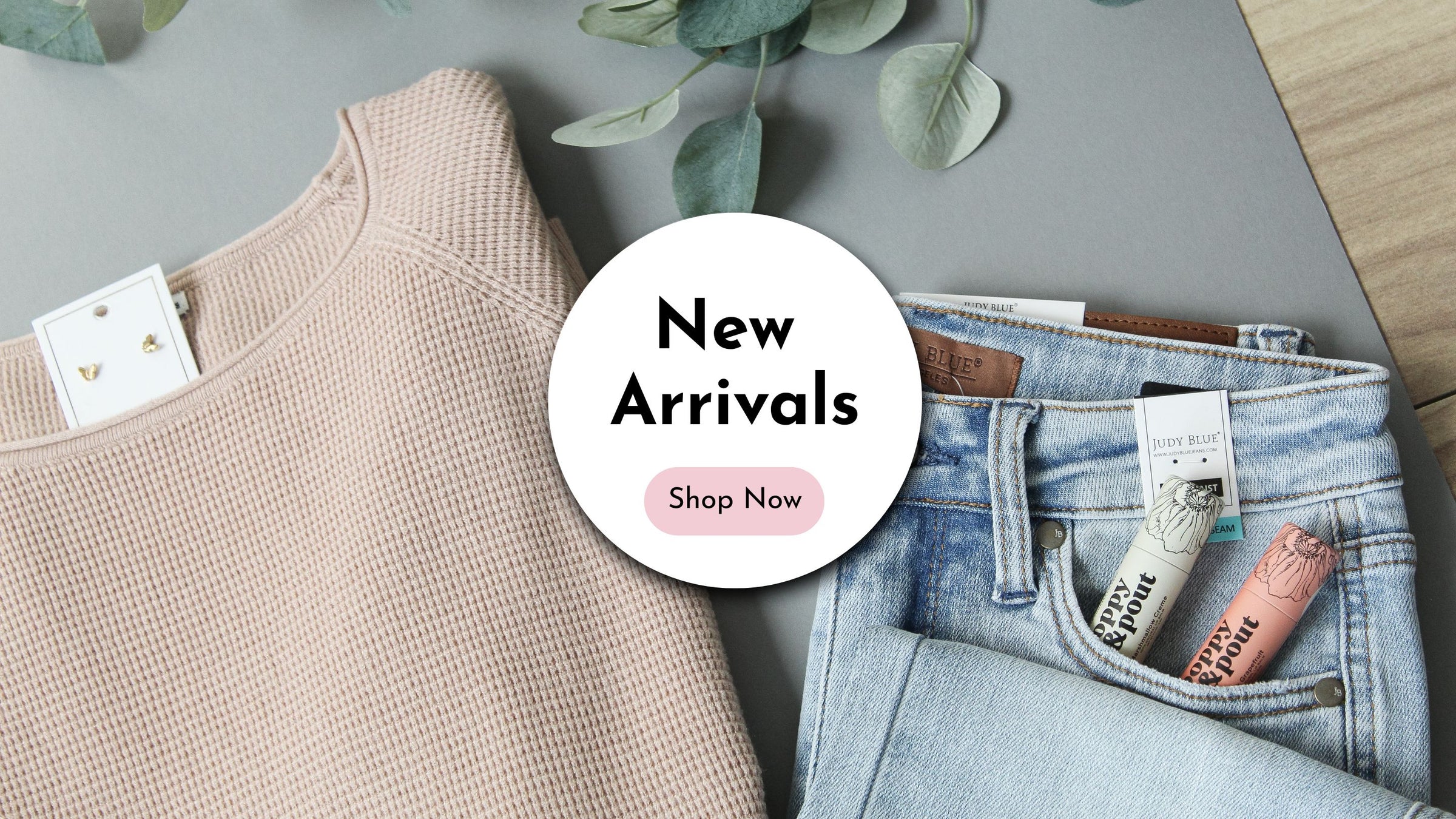 New arrivals clothing with 'Shop Now' button on a gray surface