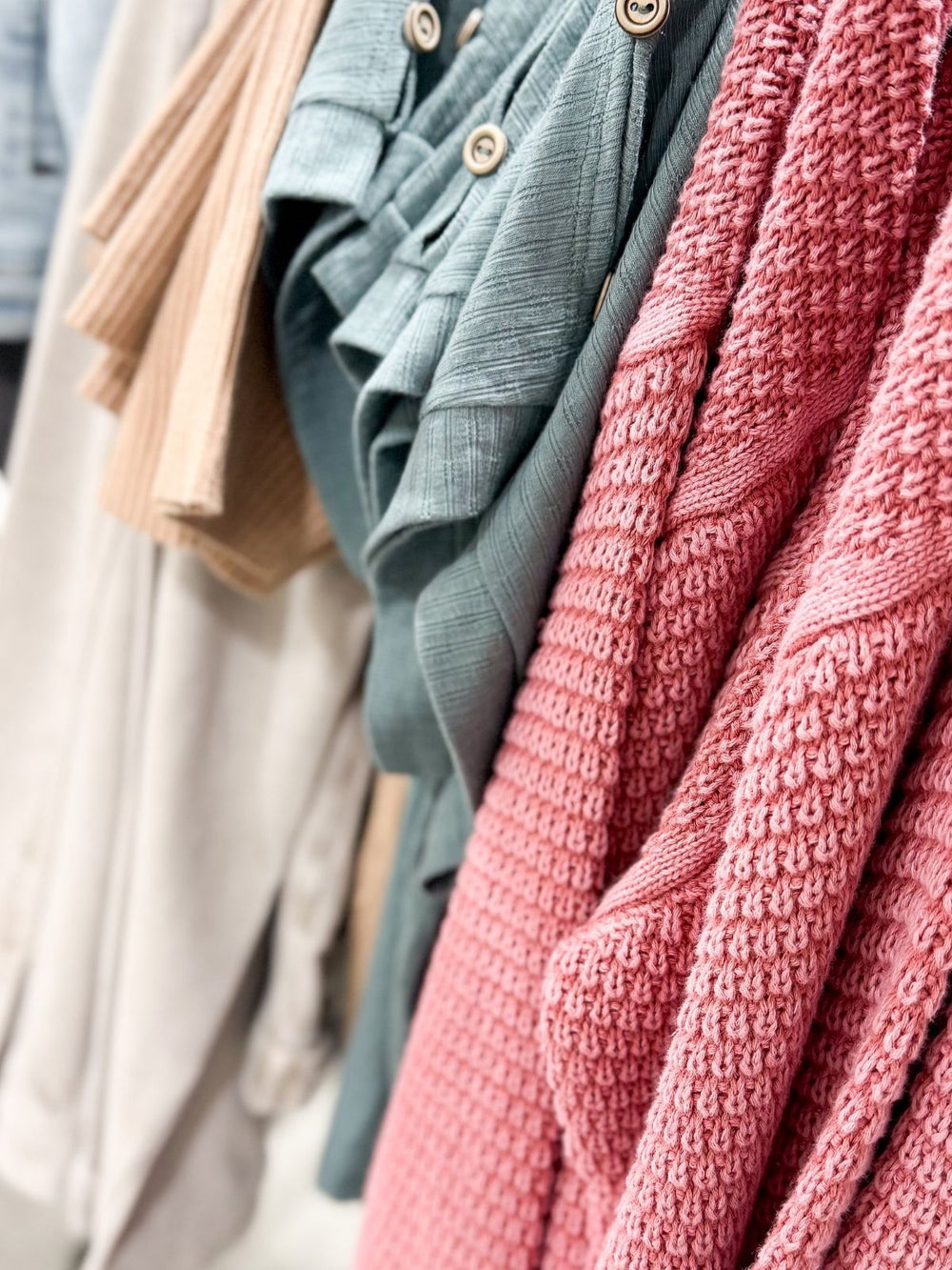 hanging items showing a mauve textured cardigan, a sage button shoulder tee, a ribbed taupe tee and a stone colored jacket.