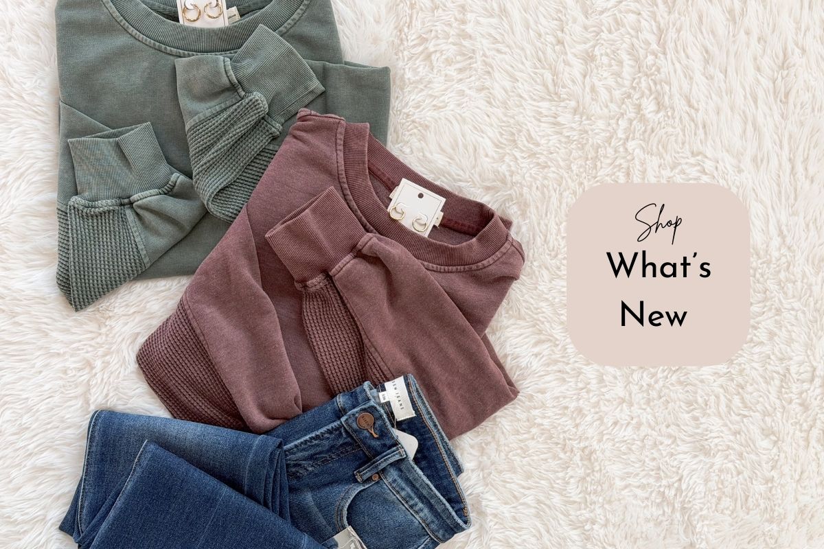 Two sweaters and a pair of jeans on a textured surface with 'Shop What's New' text.