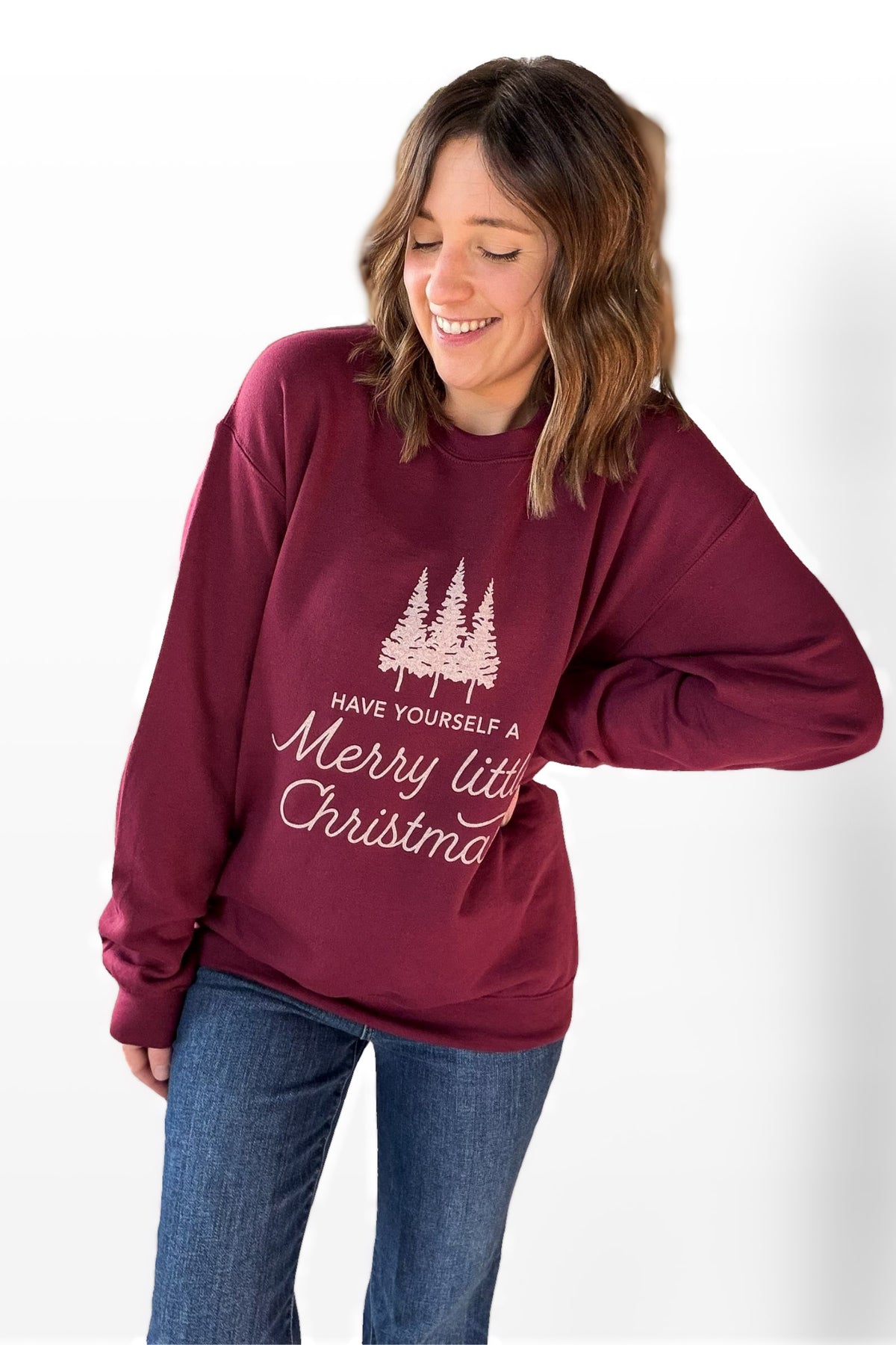 Woman wearing a maroon sweatshirt with Christmas text and tree design on a white background