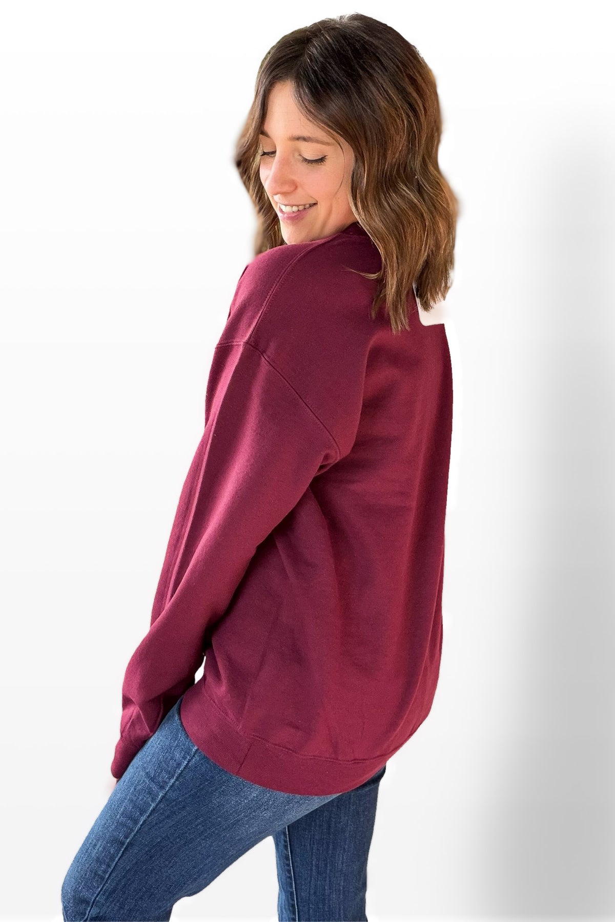 Woman wearing a maroon sweatshirt and blue jeans on a white background