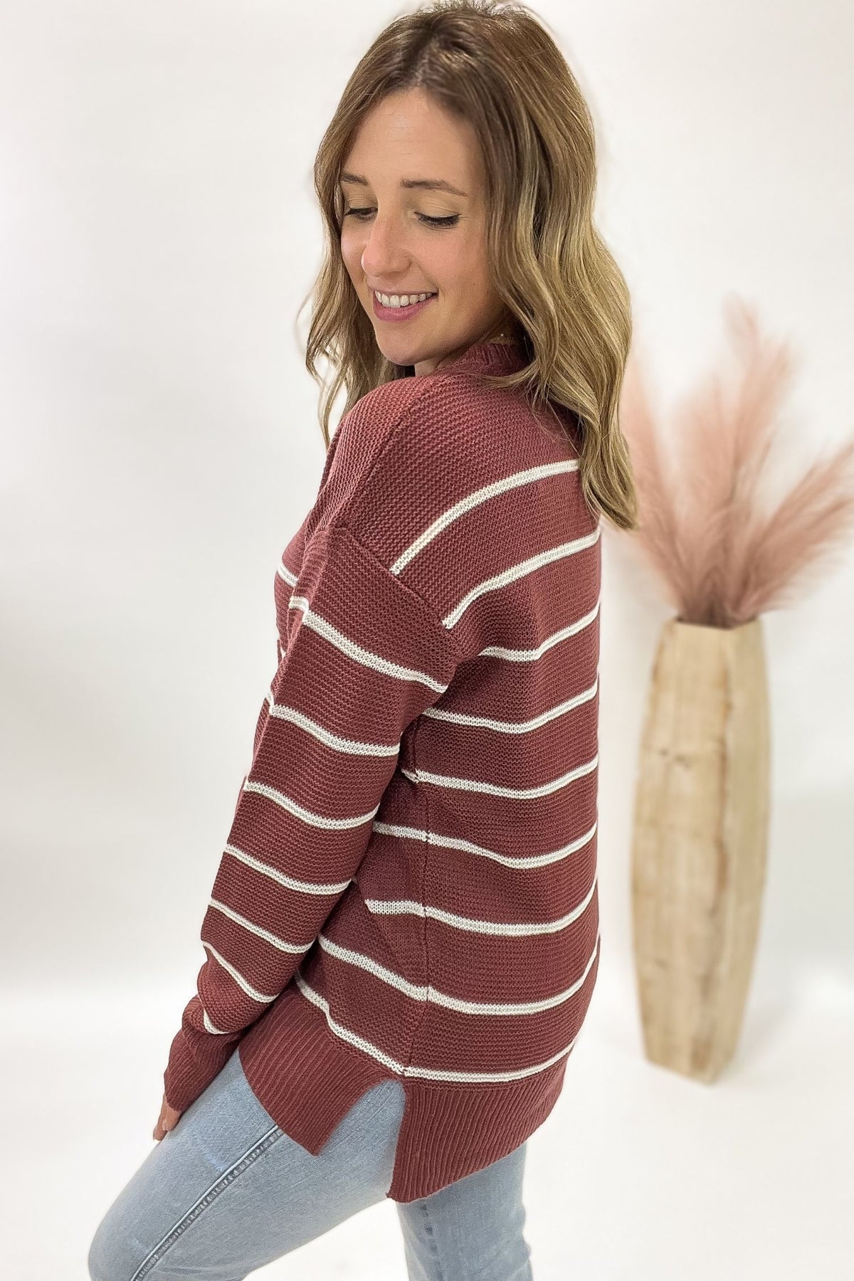 Woman wearing a striped sweater with a white background and decorative vase.