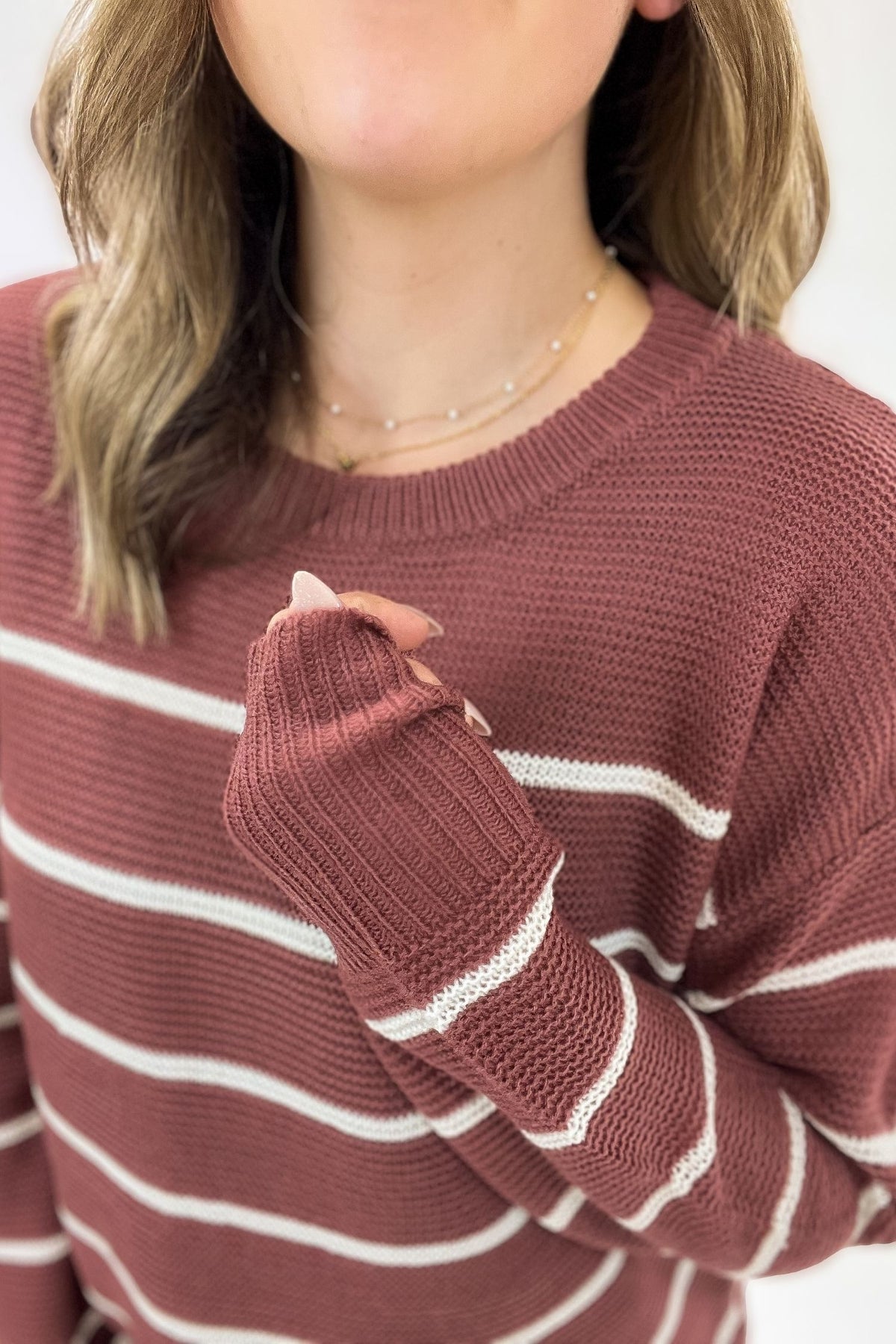Close-up of a person wearing a marsala and white striped sweater with a neutral background
