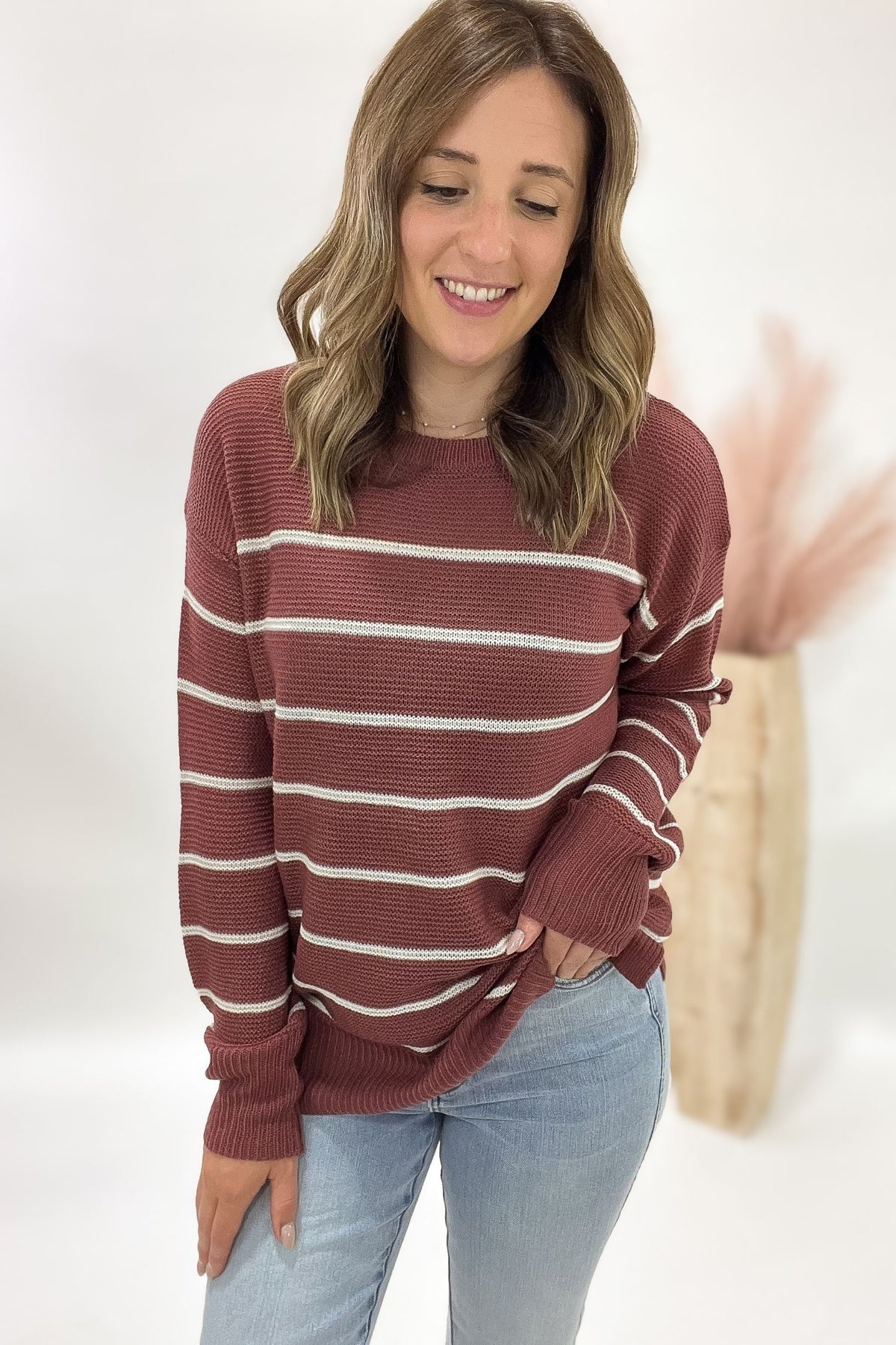 Woman wearing a marsala sweater with white stripes and light blue jeans against a white background