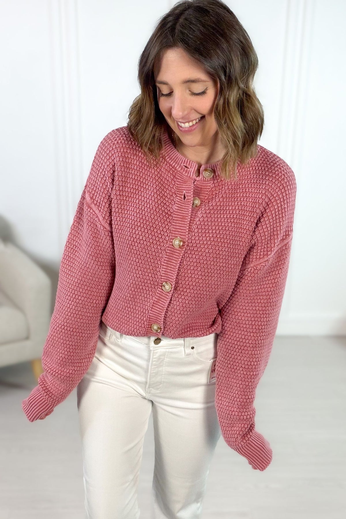 Woman wearing a mauve textured cardigan buttoned with neutral buttons indoors.