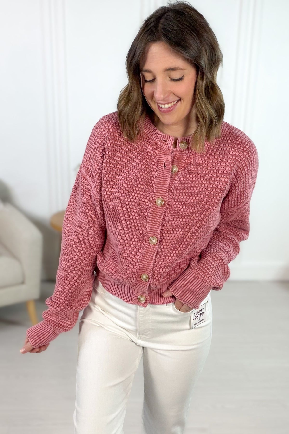 Woman wearing a mauve textured cardigan with neutral buttons indoors.
