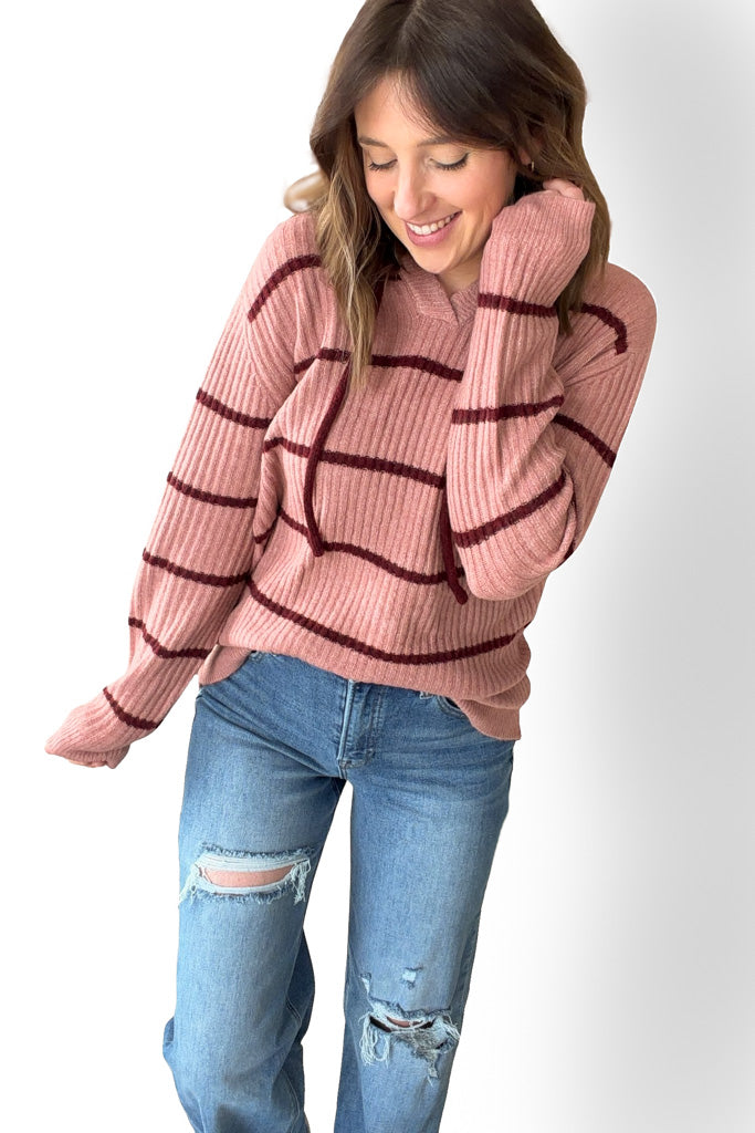 Woman wearing a mauve sweater with red stripes and blue jeans on a white background