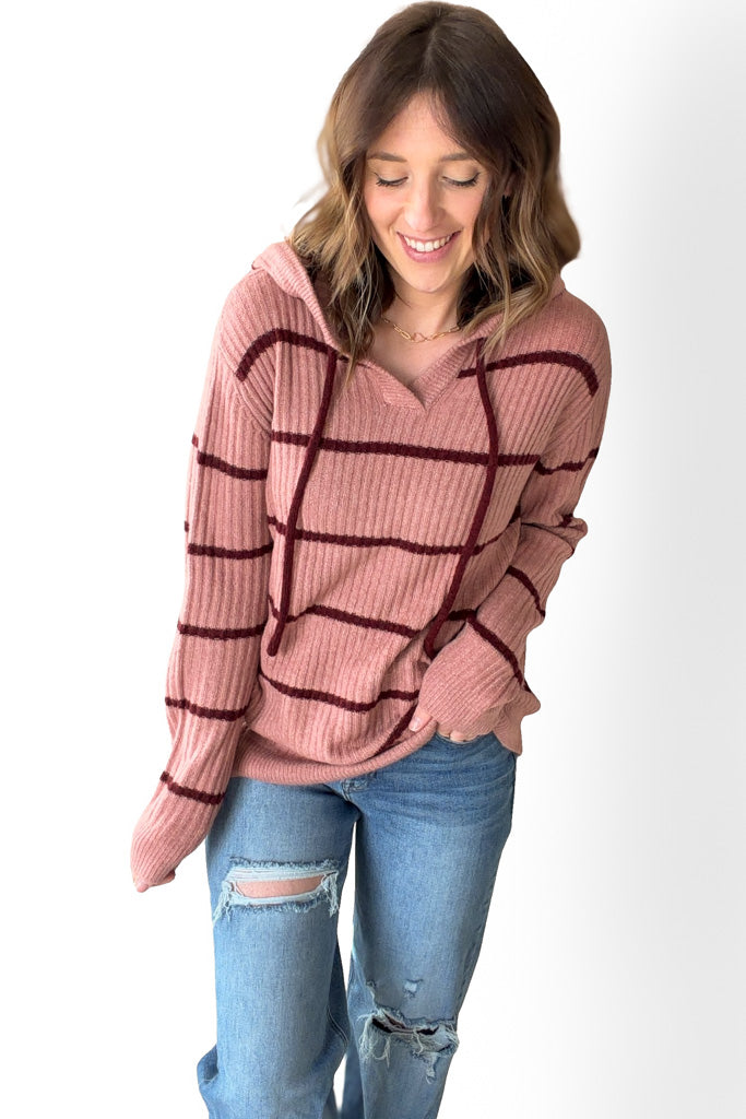 Woman wearing a mauve sweater with black stripes and ripped jeans on a white background