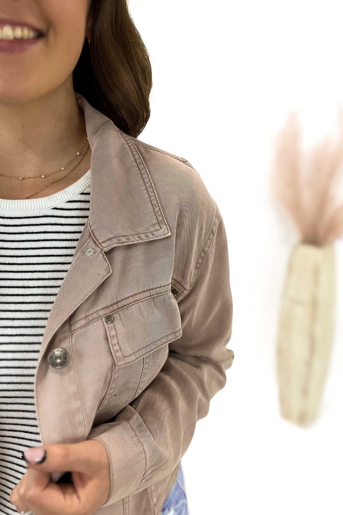 Person wearing a dusty mauve jacket over a striped shirt on a white background