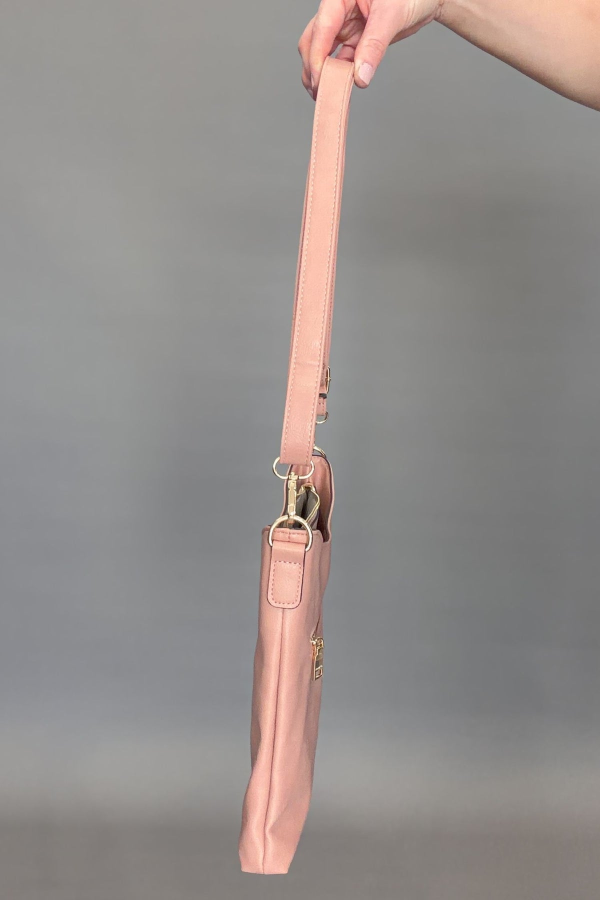 Mauve handbag with strap held by a hand against a gray background
