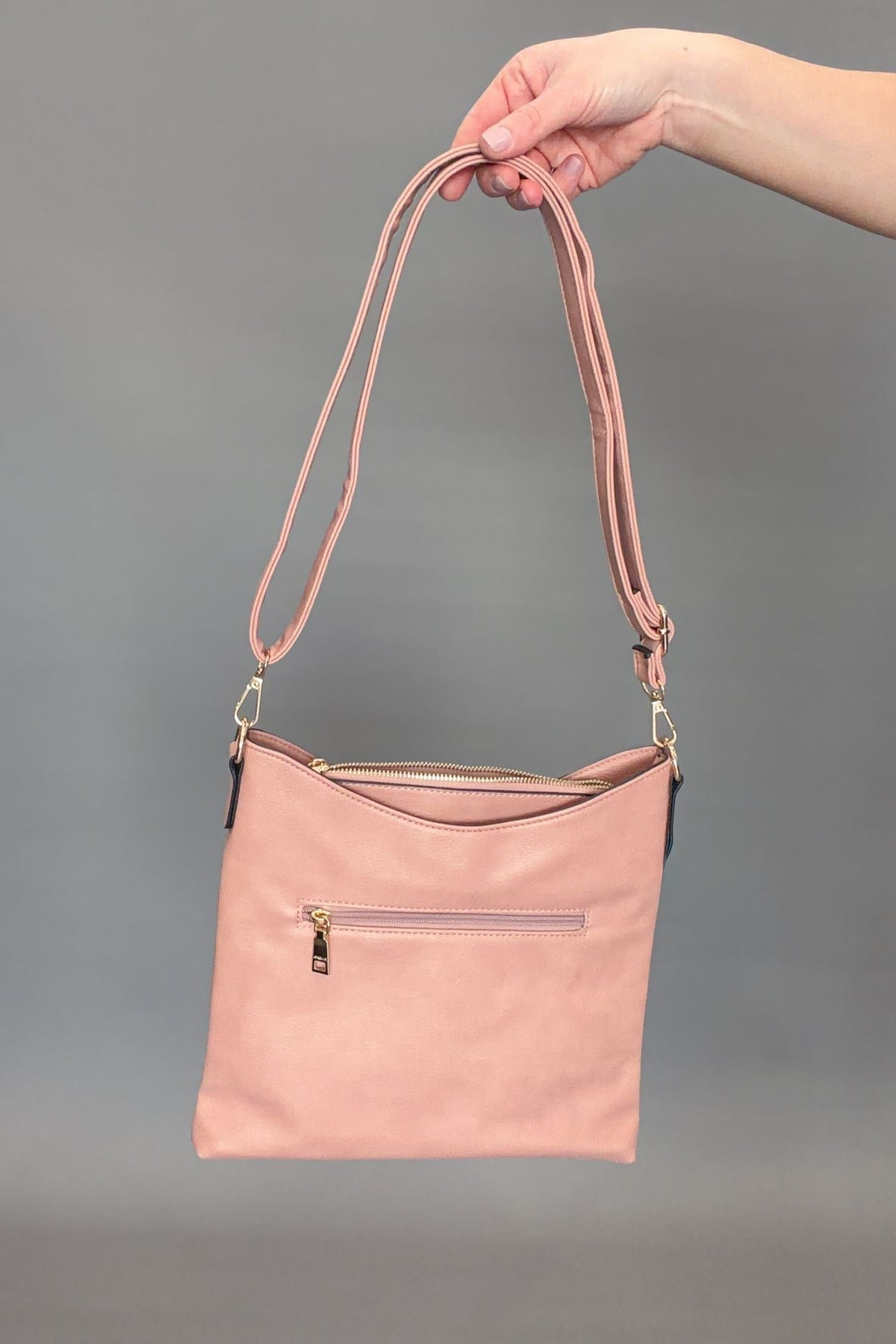 Mauve handbag held by a hand against a gray background
