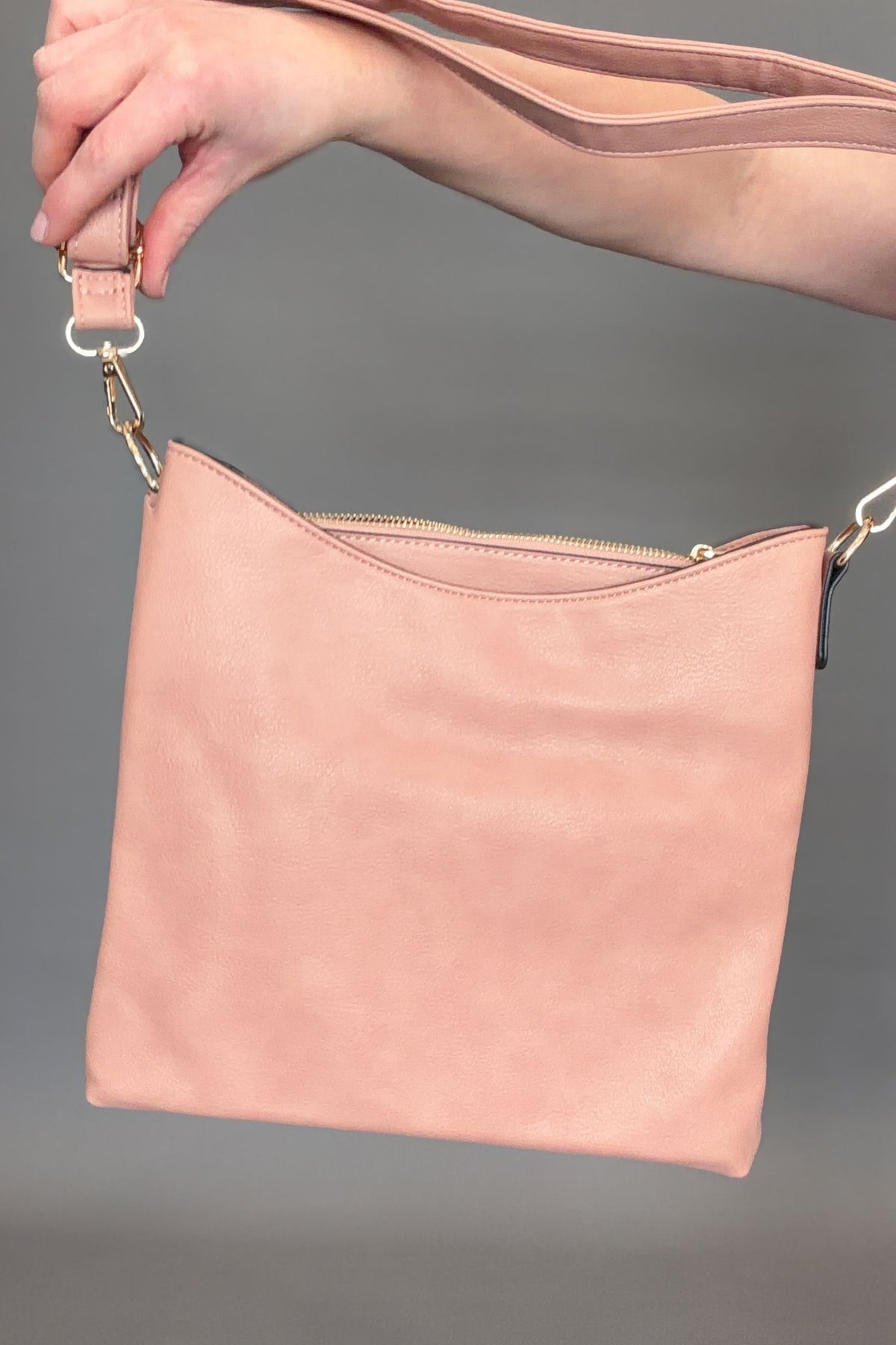Mauve handbag held by a hand against a gray background