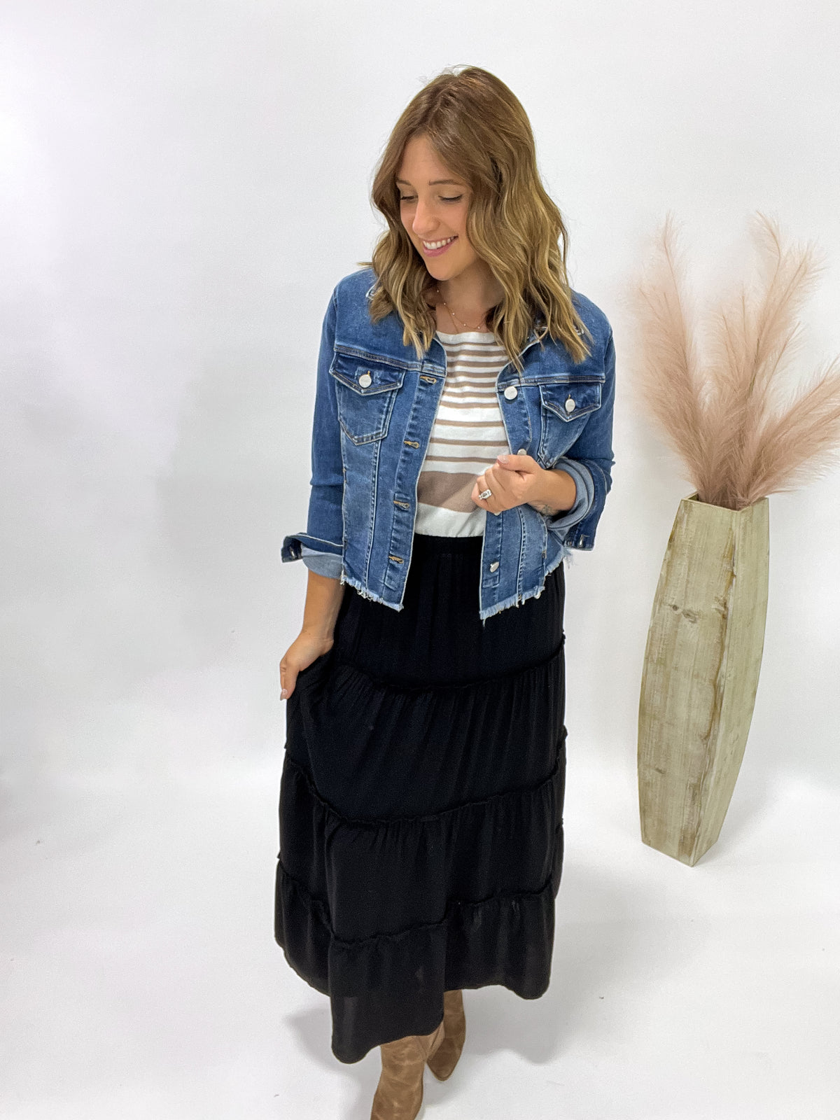 Woman wearing a denim jacket, striped shirt, and black tiered skirt on a white background