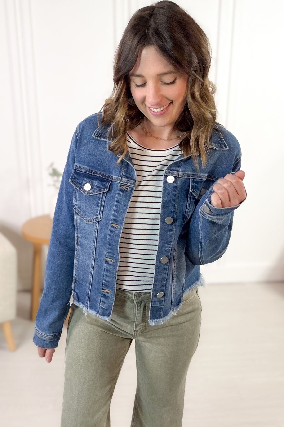 Woman wearing a blue denim jacket, striped shirt, and green pants indoors.