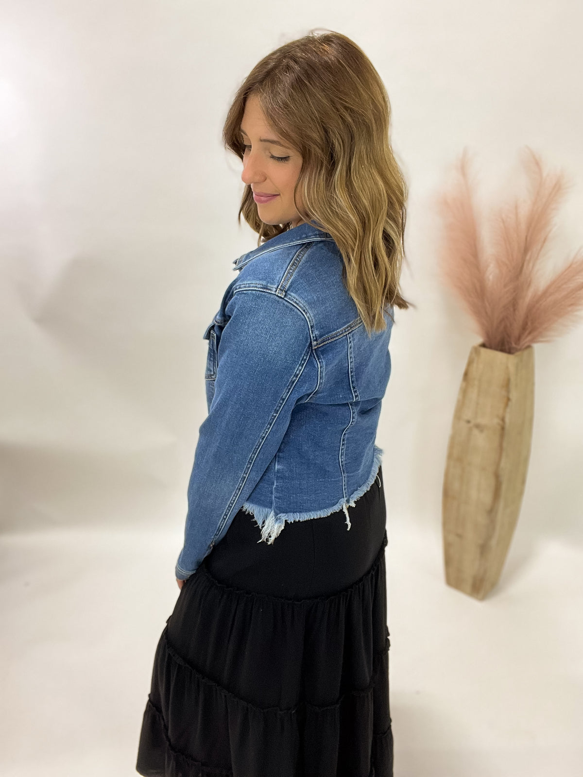 Woman wearing a denim jacket and black dress against a white background with decorative elements.