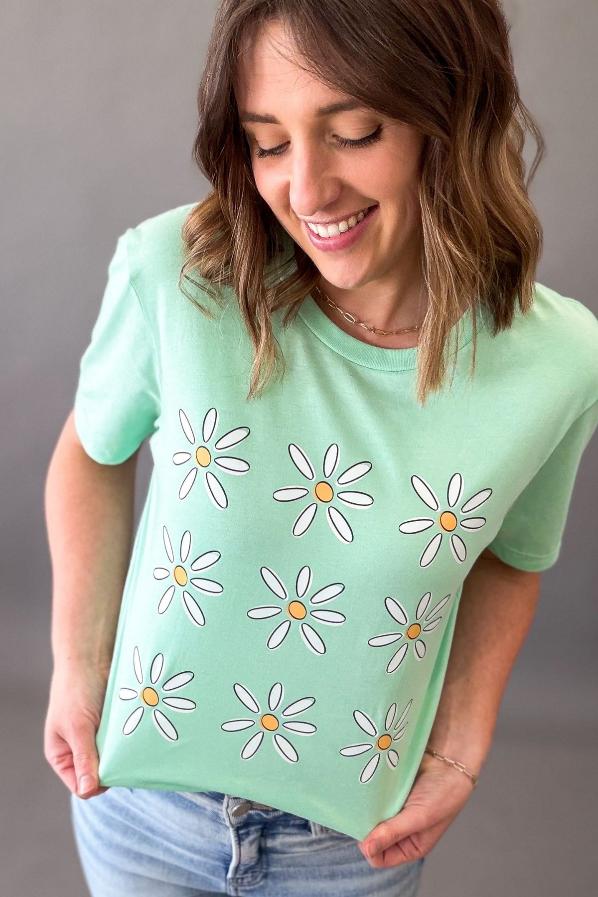 Woman wearing mint green daisy flower graphic tee with light wash denim jeans 