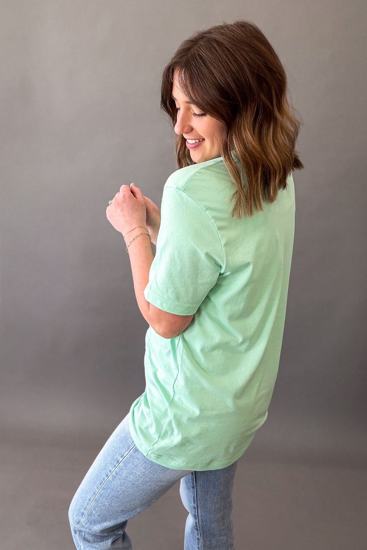Woman wearing mint green daisy flower graphic tee with light wash denim jeans showing the back details