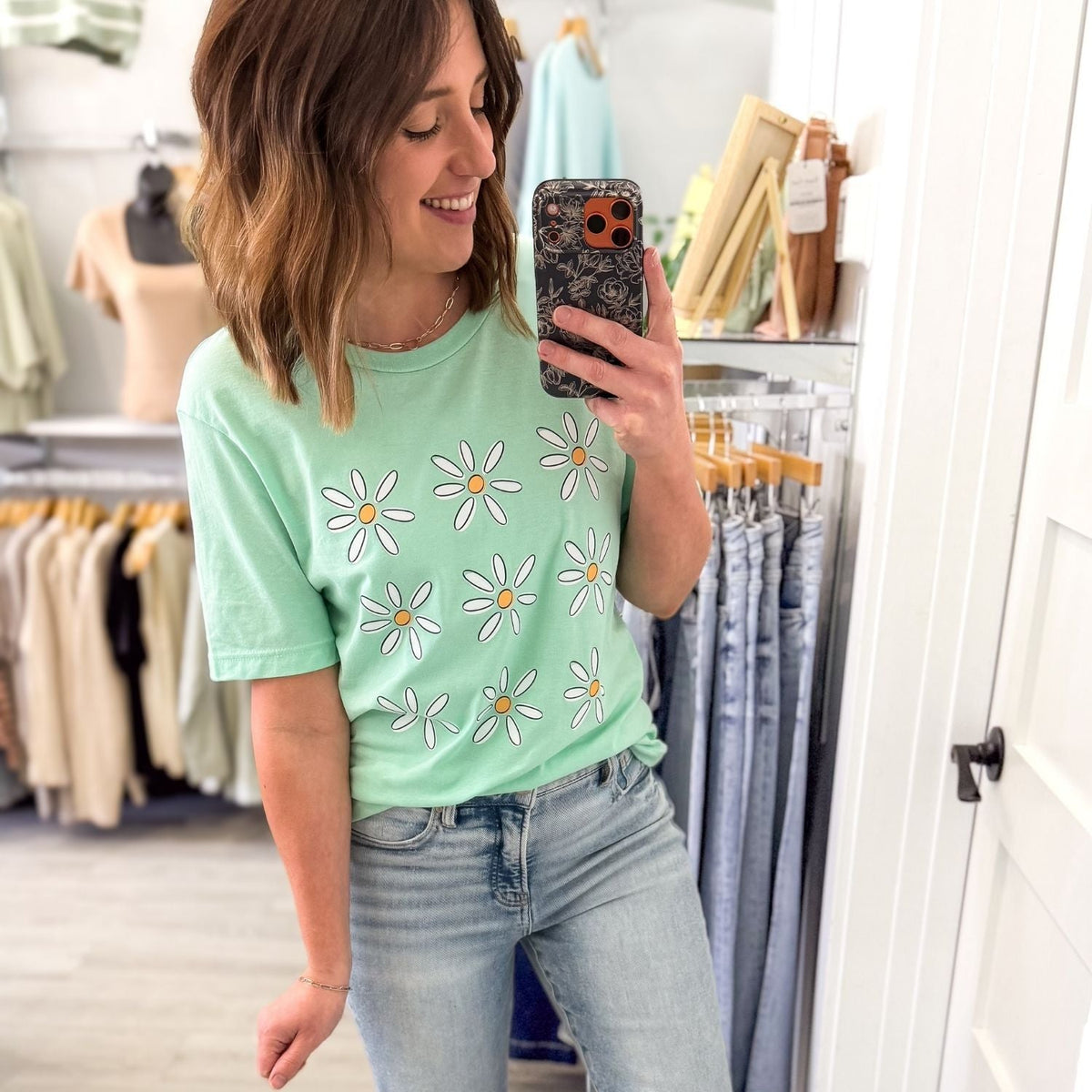 Woman taking a selfie wearing mint green daisy flower graphic tee with light