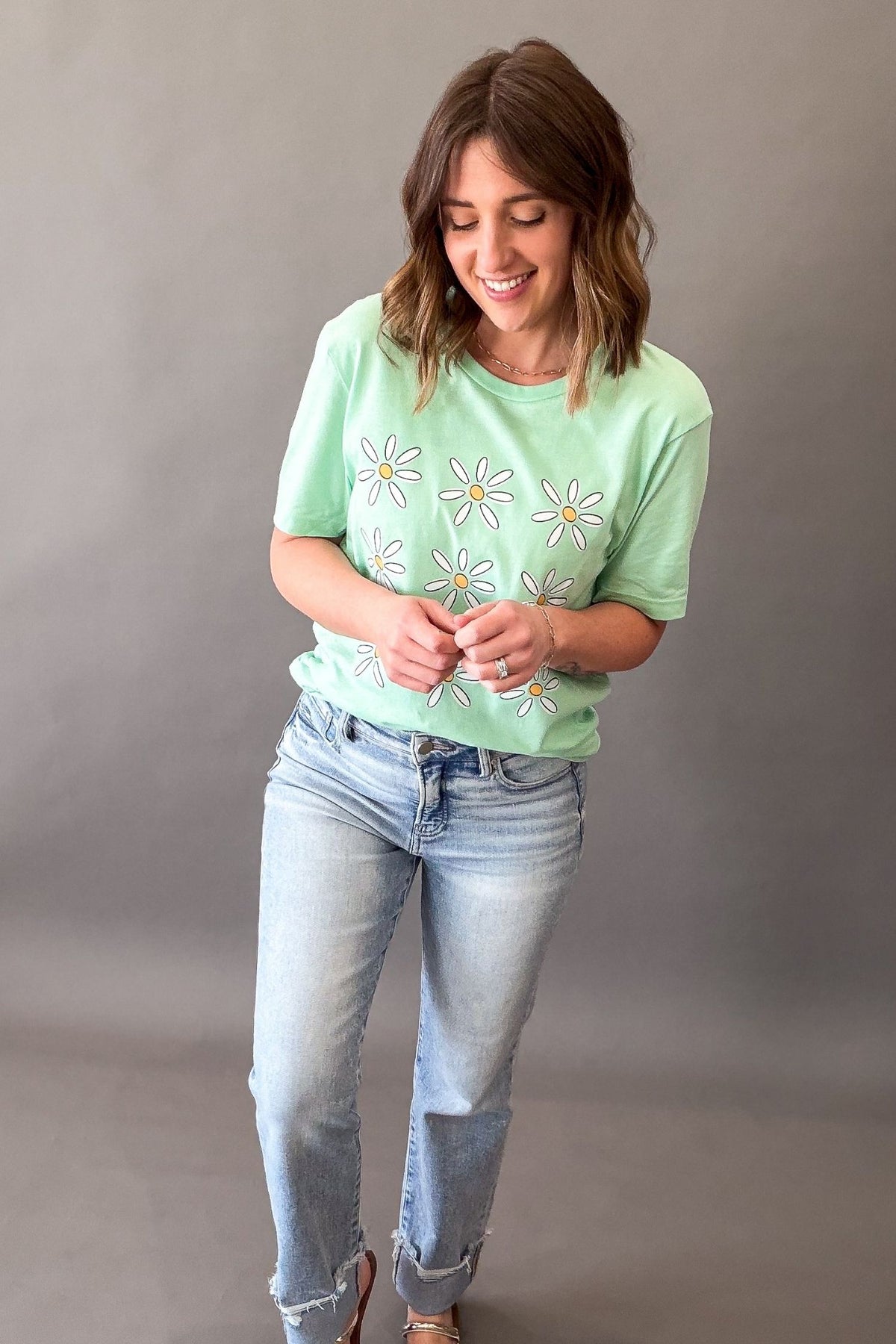 Woman wearing mint green daisy flower graphic tee with light wash denim jeans 