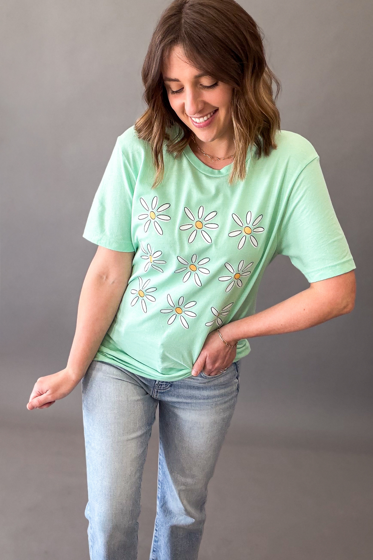 Woman wearing mint green daisy flower graphic tee with light wash denim jeans 