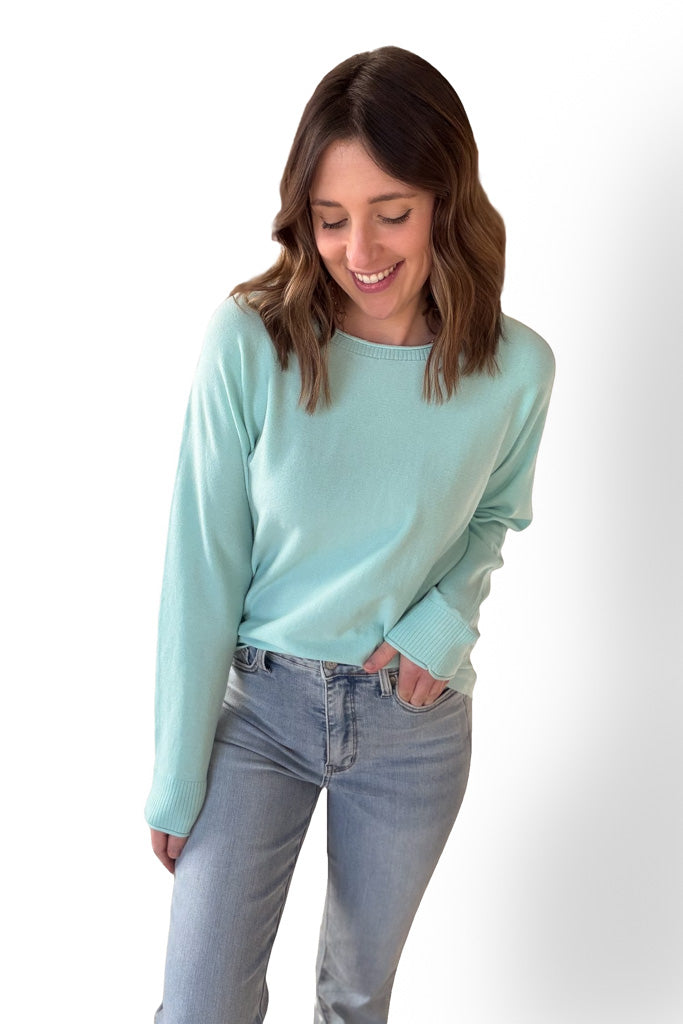 Woman wearing a mint sweater with blue jeans on a white background