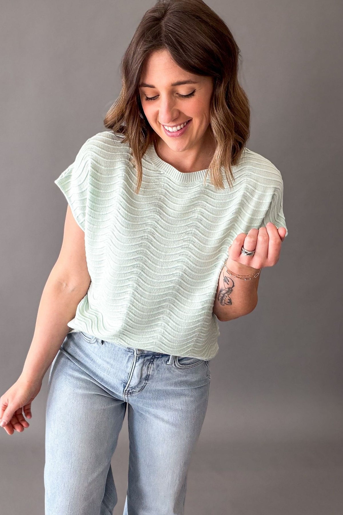 Woman wearing a light mint textured top and blue jeans against a gray background