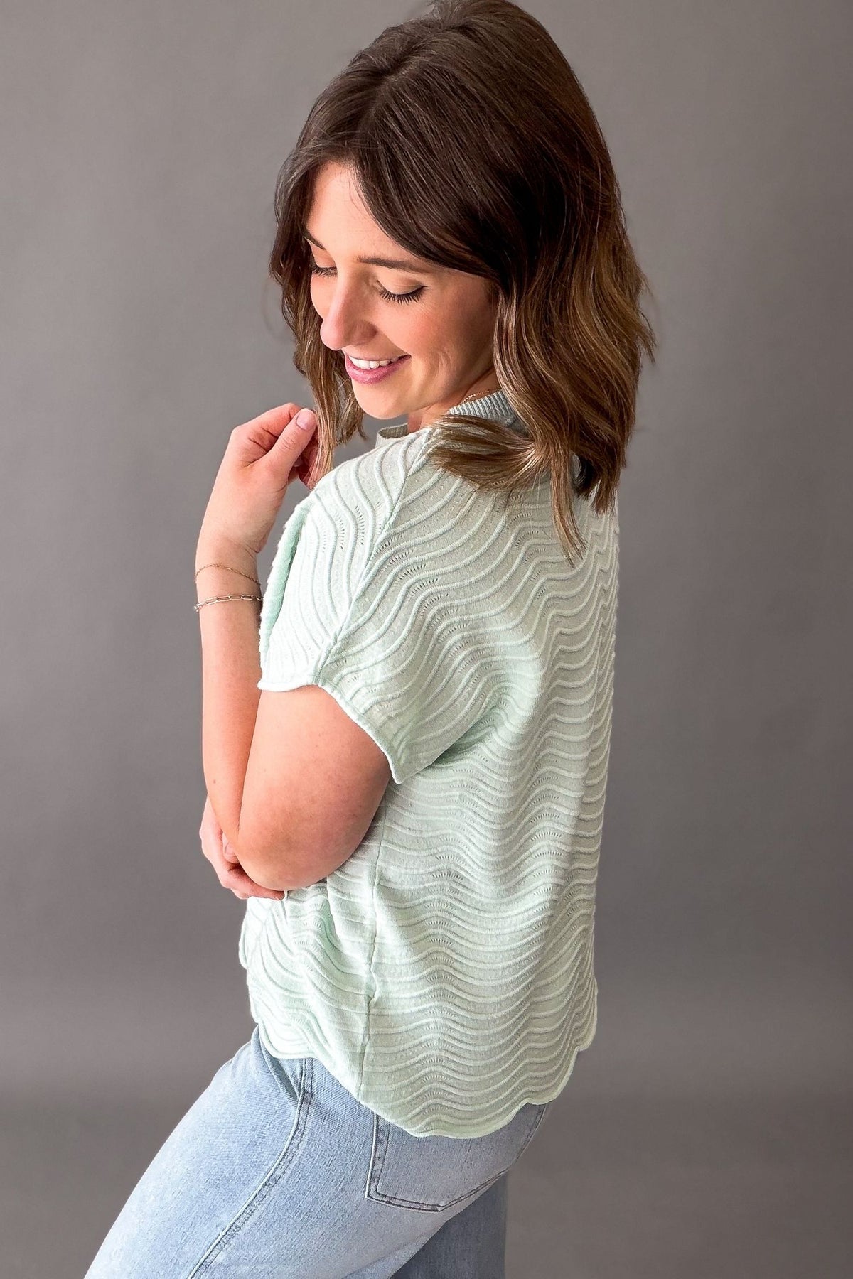 Woman wearing a light mint textured shirt and blue jeans against a gray background