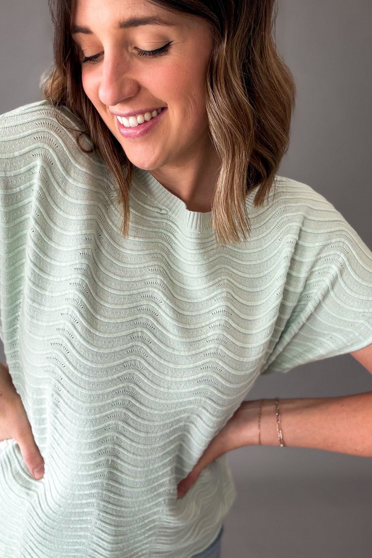 Woman wearing a light mint textured sweater against a neutral background