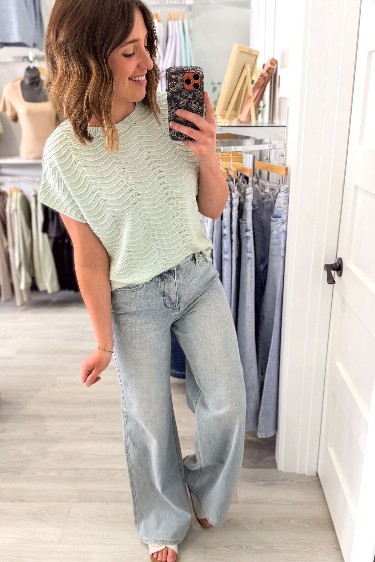 Woman taking a mirror selfie wearing a light mint short sleeve and blue jeans in a clothing store.