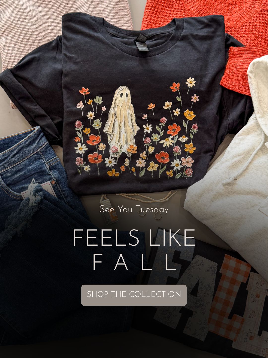 A dark charcoal graphic T-shirt laid flat on top of other clothing, featuring a ghost surrounded by colorful autumn flowers. Large overlaid text reads 'FEELS LIKE FALL' with a 'SHOP THE COLLECTION' button below.