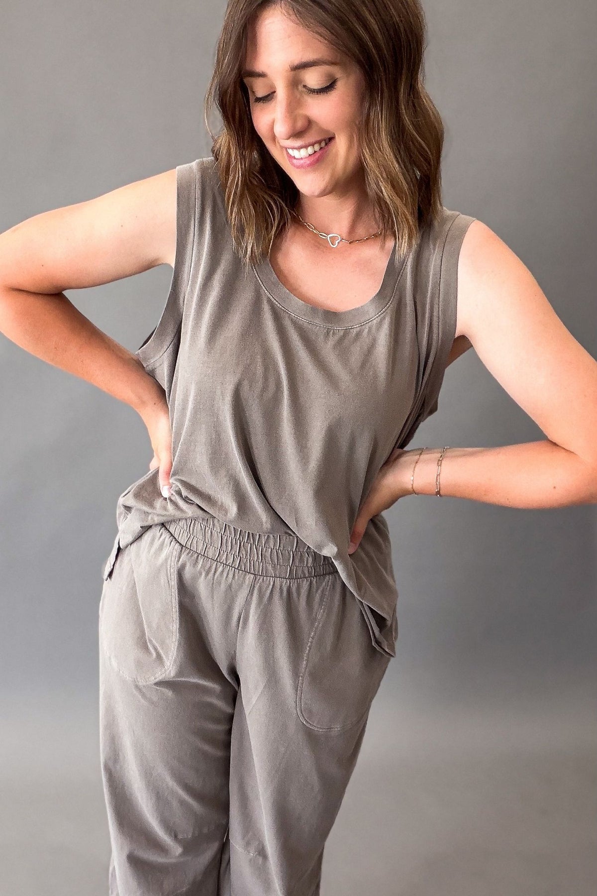 A woman modeling a matching two-piece lounge set in a mocha color, featuring a sleeveless top and matching pants with an elastic waistband.