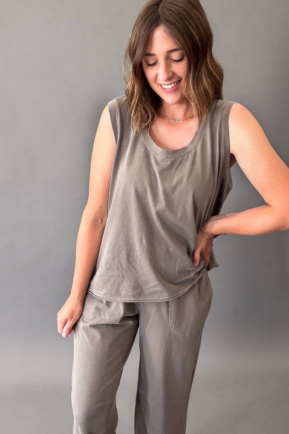 A woman modeling a matching two-piece lounge set in a muted mocha color, featuring a sleeveless scoop-neck top and coordinating pants, set against a plain gray studio background.