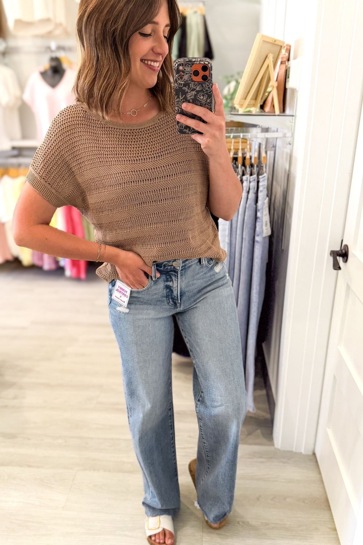 woman taking a selfie wearing a short sleeve mocha crew neck pointelle sweater and blue jeans in a clothing boutique