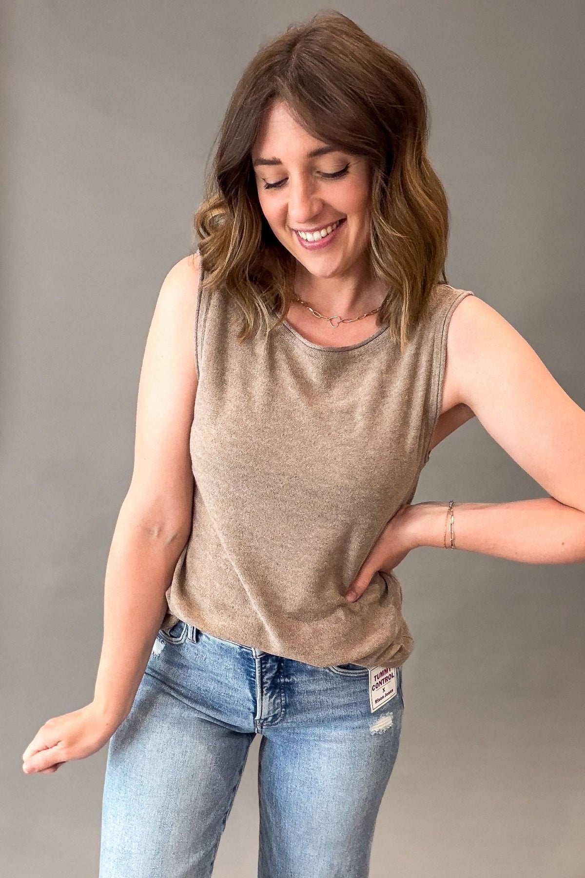 Woman wearing a mocha tank top and blue jeans against a gray background