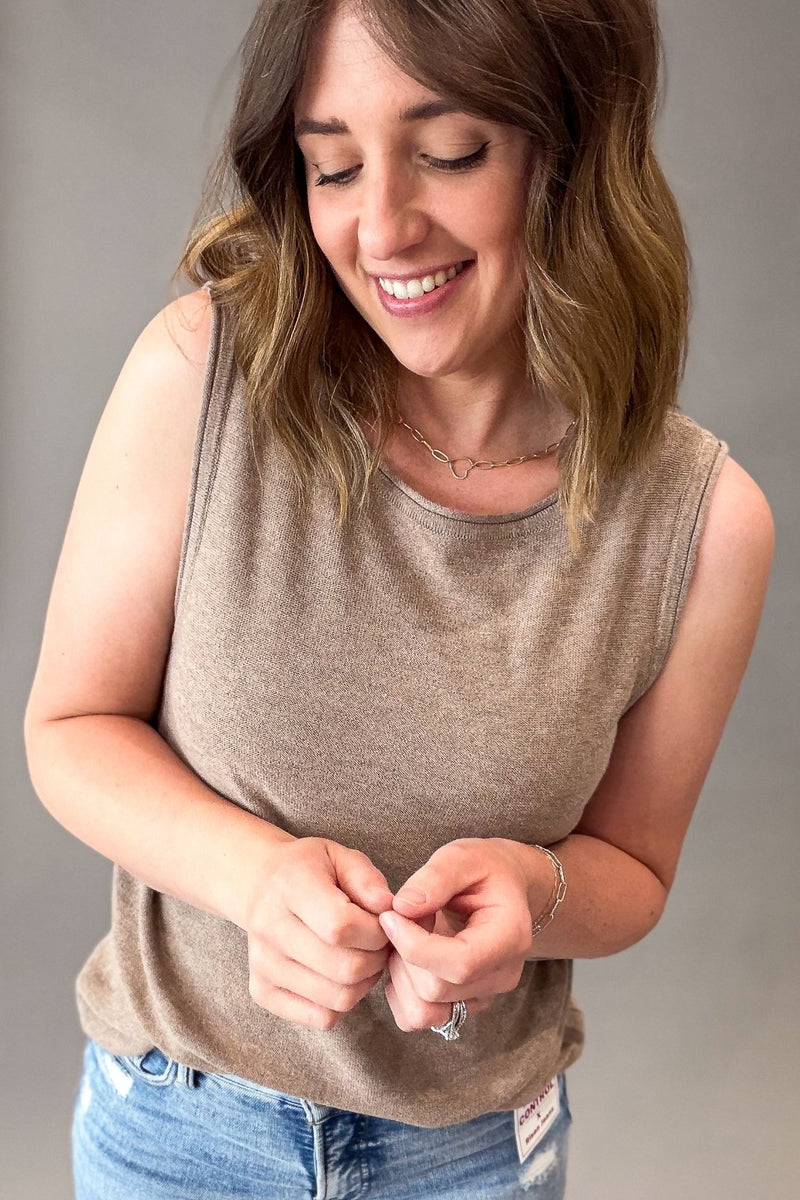 Woman wearing a mocha sleeveless top and blue jeans against a gray background