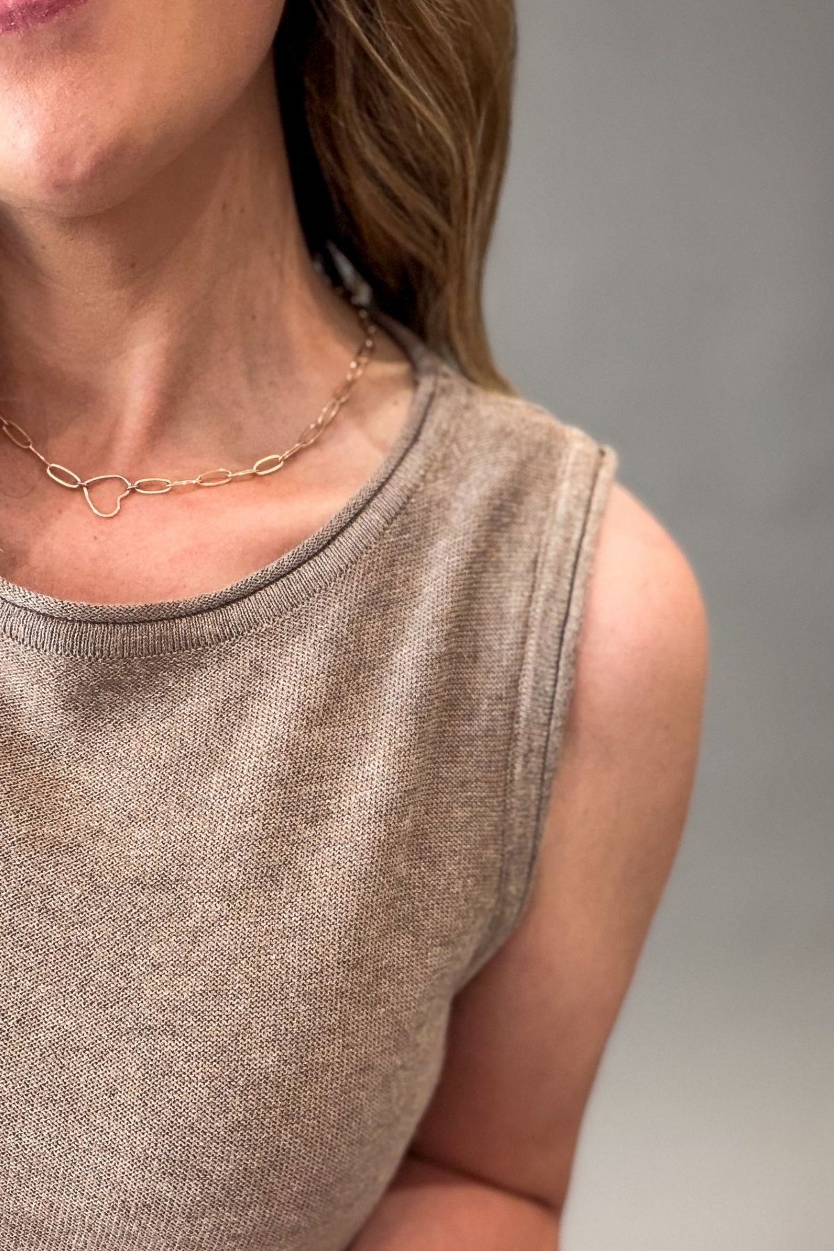 Close-up of a person wearing a mocha sleeveless top and gold necklace on a gray background