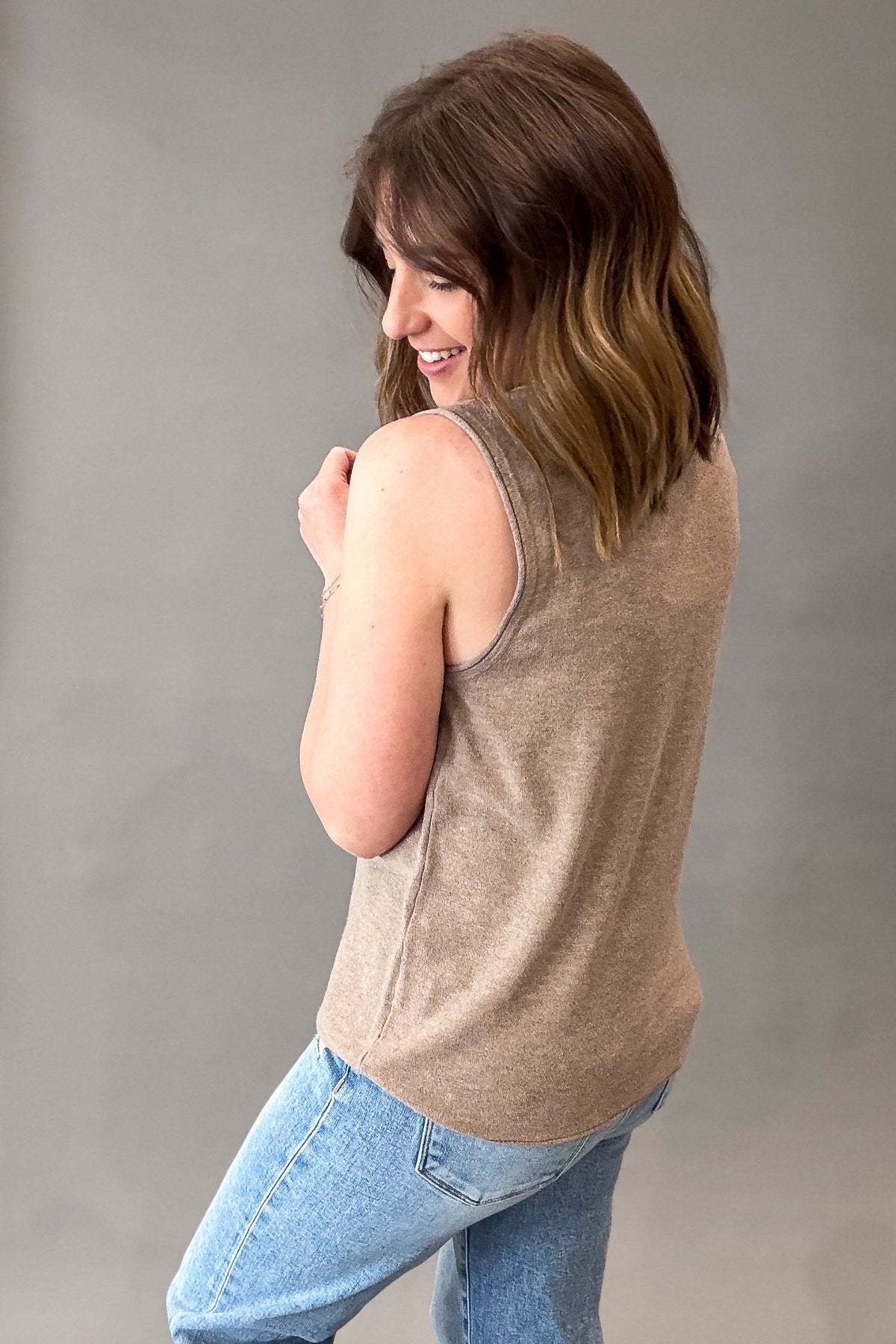 Woman wearing a mocha tank top and blue jeans against a gray background