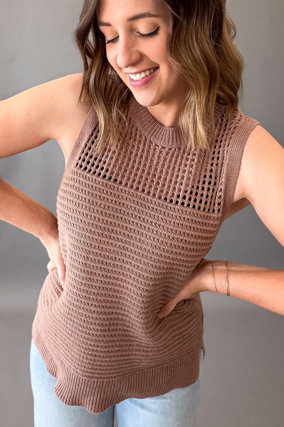 woman wearing a mocha tank untucked with light wash jeans on a grey background