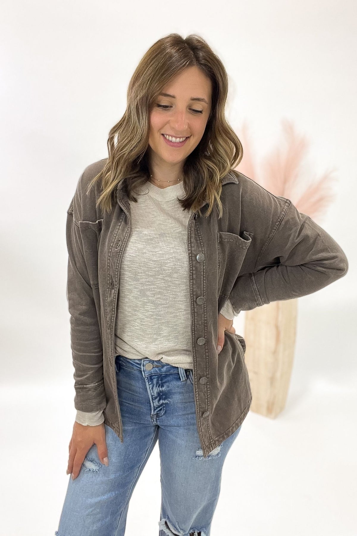 Woman wearing a brown jacket over a white shirt and blue jeans on a white background