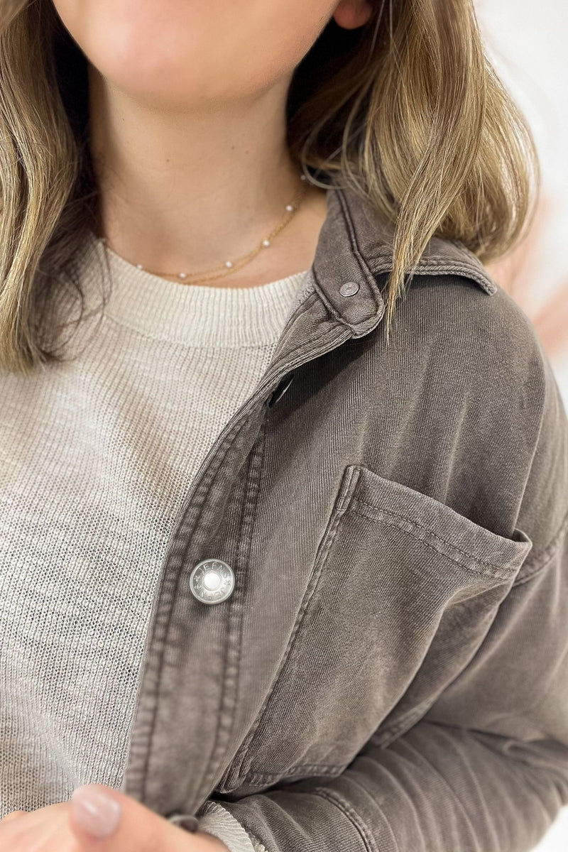Close-up of a person wearing a gray button-up shirt over a light gray sweater.