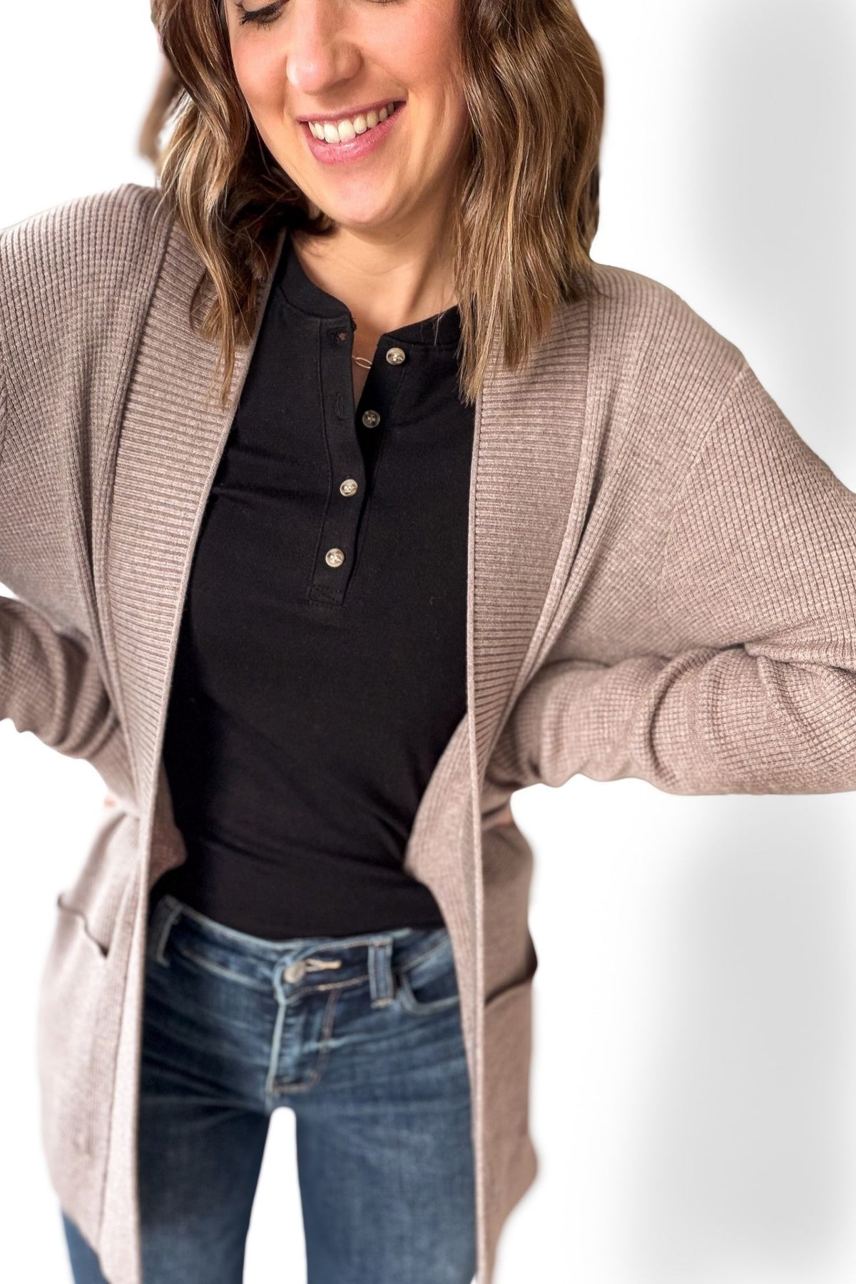 Woman wearing a beige cardigan over a black shirt and blue jeans on a white background